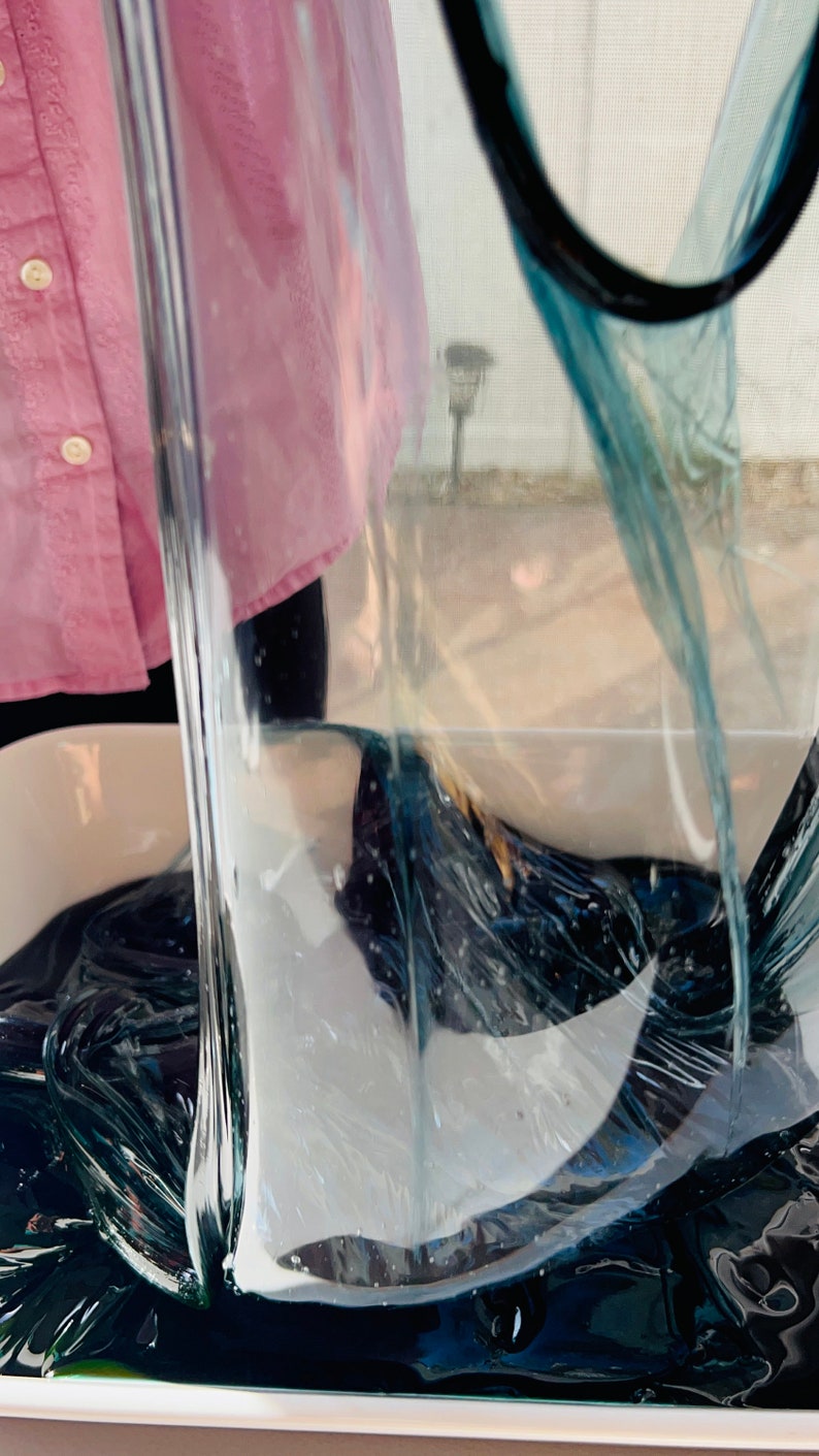 May include: A person is holding a clear plastic sheet over a container of dark blue slime. The slime is thick and gooey, and it is filling the container.