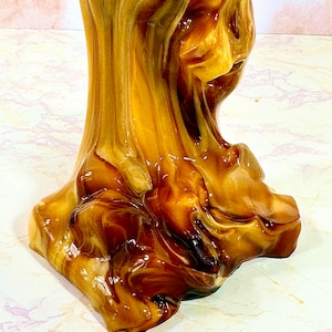 May include: A close-up of a brown and gold resin sculpture with a swirled, abstract design. The sculpture has a smooth, glossy finish.