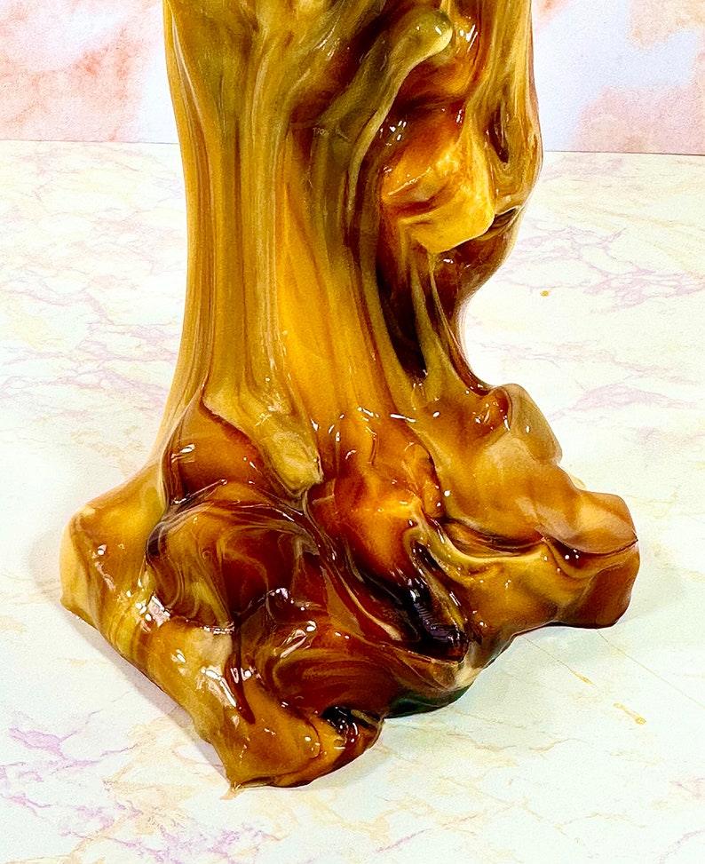 May include: A close-up of a brown and gold resin sculpture with a swirled, abstract design. The sculpture has a smooth, glossy finish.