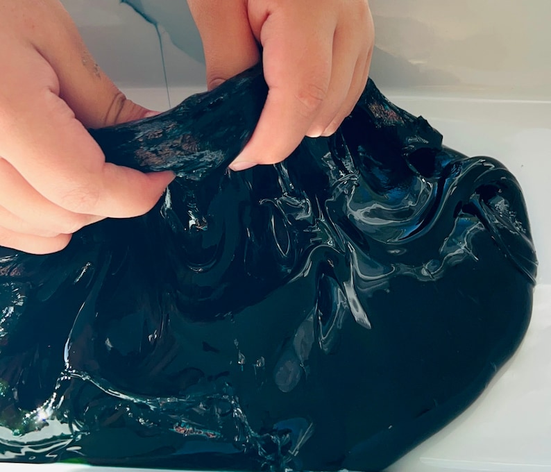 May include: A close-up of black slime being stretched and pulled by hands. The slime is shiny and has a smooth texture.