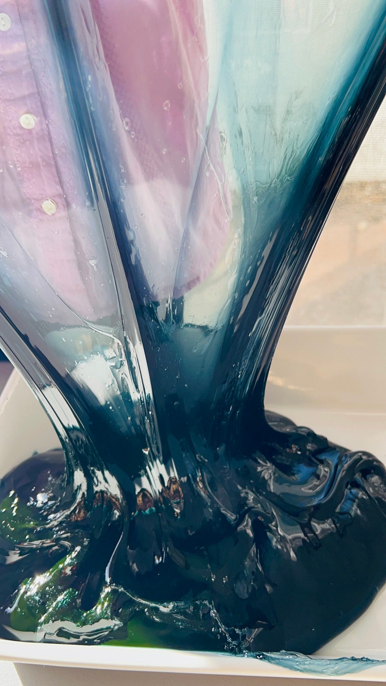May include: A close-up of dark blue slime being poured into a white container. The slime is thick and gooey, and it has a slightly iridescent sheen.