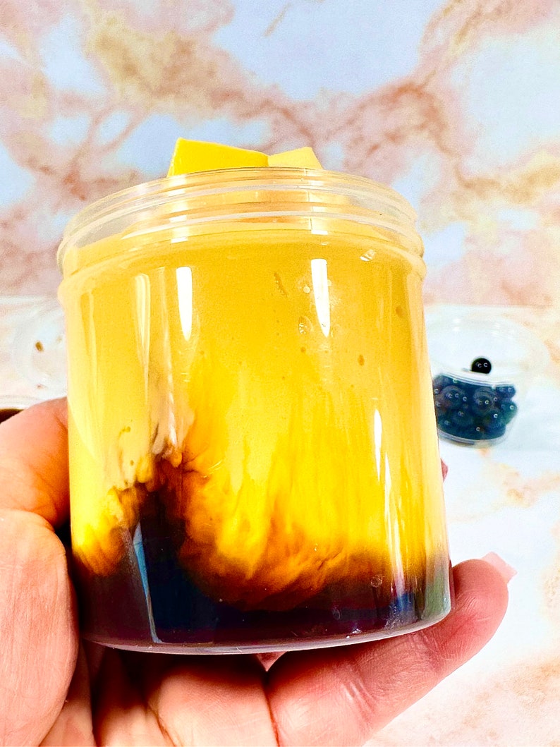 May include: A clear glass jar filled with a layered dessert. The bottom layer is a dark brown liquid, the middle layer is a light yellow custard, and the top layer is a light brown foam.