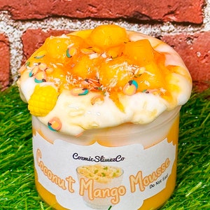 May include: A clear jar of yellow and white coconut mango mousse slime with a white label that reads "Cosmic Slime Co. Coconut Mango Mousse Do Not Eat".