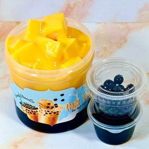 May include: A clear plastic container filled with yellow mango jelly and topped with a layer of mango pudding. A smaller clear plastic container with a black lid holds black tapioca pearls. The label on the larger container reads "Thai Tea Do Not Eat".