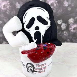 Könnte beinhalten: Ein weißes Glas Slime mit roter und schwarzer Glitzer-Beschichtung. Der Slime ist mit einem weißen Telefon und einer schwarzen Maske mit einem weißen Geistergesicht bedeckt. Das Glas hat ein weißes Etikett mit dem Text "No you hang up first!" und einem Schwarzweißbild des Geistergesichts.