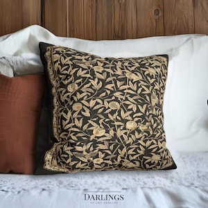 Könnte beinhalten: Ein dekoratives quadratisches Kissen mit schwarzem Hintergrund und beigem Blumenmuster. Das Kissen hat einen schwarzen Rand und liegt auf einem weißen Bett mit anderen Kissen. Der Text "DARLINGS OF ART DESIGNS" ist unten zu sehen.