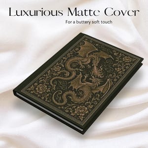 May include: A black hardback journal featuring a gold-toned illustration of two dragons intertwined with floral patterns on the front cover. The text "Luxurious Matte Cover" and "For a buttery soft touch" is printed in black above the journal.
