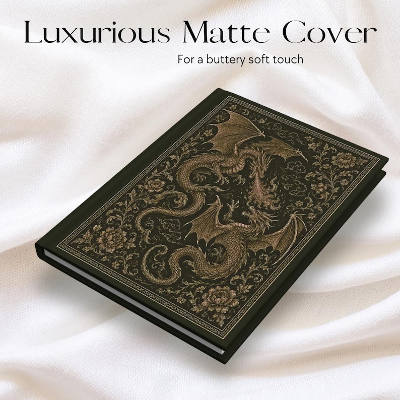 May include: A black hardback journal featuring a gold-toned illustration of two dragons intertwined with floral patterns on the front cover. The text "Luxurious Matte Cover" and "For a buttery soft touch" is printed in black above the journal.