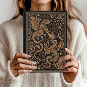May include: A black hardback journal featuring an intricate gold-coloured illustration of two dragons facing each other, surrounded by detailed floral patterns and swirling cloud motifs, all enclosed within a decorative rectangular border.