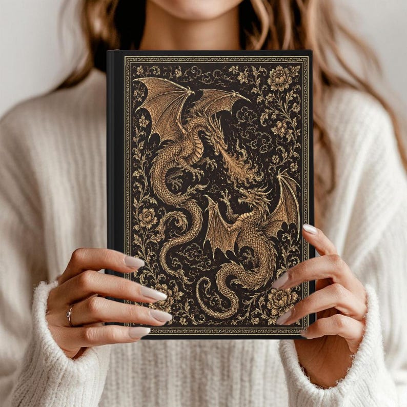 May include: A black hardback journal featuring an intricate gold-coloured illustration of two dragons facing each other, surrounded by detailed floral patterns and swirling cloud motifs, all enclosed within a decorative rectangular border.