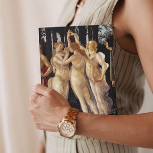 May include: A rectangular notebook featuring a reproduction of the Three Graces from Botticelli's Primavera painting. The artwork depicts three figures in sheer, flowing garments dancing against a dark, wooded background with golden highlights.