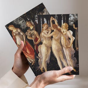 May include: Two rectangular notebooks featuring a reproduction of Botticelli's Primavera painting on the covers. The artwork displays three figures dancing in sheer white garments against a dark forest background, with another figure in a red dress.