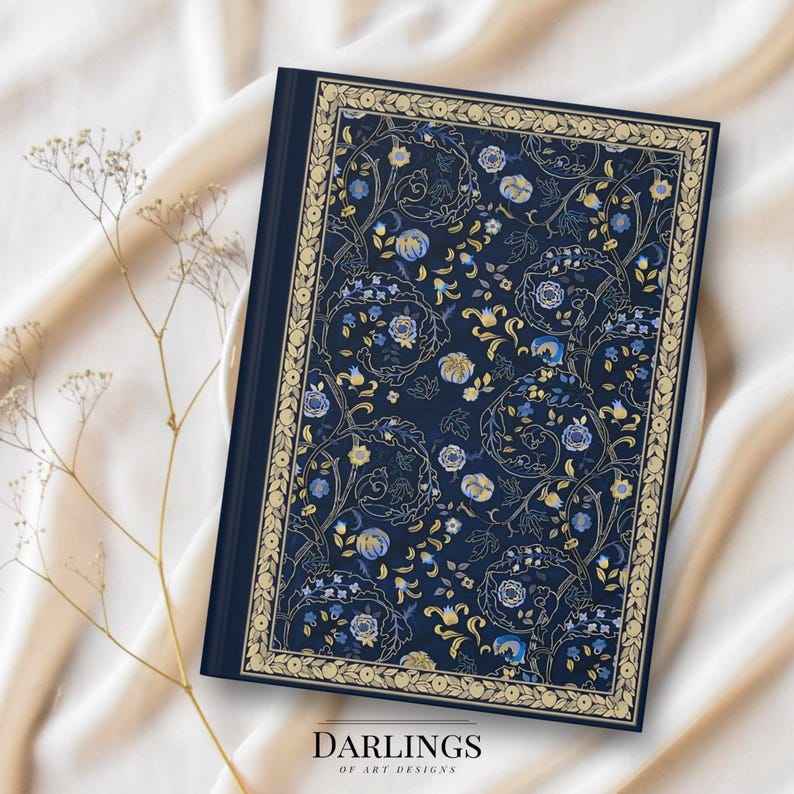 May include: A navy blue journal with a floral pattern in gold and blue. The cover features a decorative border and the text "DARLINGS OF ART DESIGNS" at the bottom. The journal is set against a cream-colored fabric.