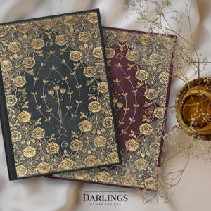 Può includere: Due diari rilegati con disegni floreali dorati su copertine nere e bordeaux. Le copertine presentano un motivo ripetitivo di rose e viti. Il testo "DARLINGS OF ART DESIGNS" è stampato nella parte inferiore dell'immagine.