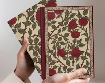 Op de afbeelding: Een hardcover boek met een crèmekleurige kaft voorzien van een herhalend patroon van donkerrode rozen, groene bladeren en doornige stengels. De voorzijde is omlijst door een decoratieve rand in goud- en bruintinten met een donkerrode rug.