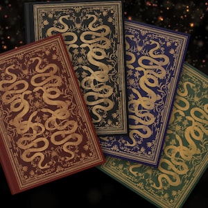 May include: A collection of hardcover books with ornate gold snake and floral designs on the covers. The books are in various colors, including burgundy, black, blue, and green, with gold accents. The covers have a vintage, antique aesthetic.