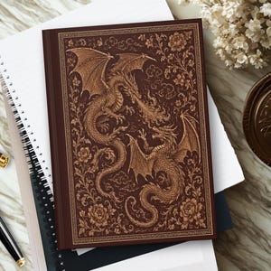 May include: A dark brown hardback journal featuring an intricate gold-toned illustration of two dragons facing each other, with one dragon breathing fire. The cover is decorated with detailed floral patterns, swirling clouds, and a thin gold border.