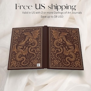 May include: A dark brown hardback art journal featuring an intricate gold-toned embossed design of two dragons intertwined with floral patterns on the front and back covers. A small square QR code is visible on the bottom right corner.