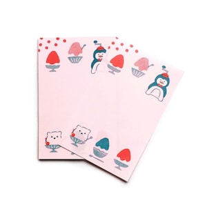 Könnte beinhalten: Zwei rosa Schreibwarenblätter mit einem sich wiederholenden Muster aus Cartoon-Pinguinen, Bären und Eisdesserts. Die Illustrationen sind in Rot, Blau und Weiß gehalten. Die Blätter sind leer und bereit zum Beschreiben.