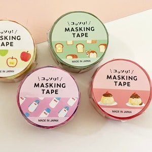 Könnte beinhalten: Vier Rollen Masking Tape mit verschiedenen Designs. Jede Rolle trägt den Text "MASKING TAPE" und japanische Schriftzeichen. Die Designs umfassen Äpfel, Brot, Pinguine mit Milchflaschen und Pudding. Hergestellt in Japan.