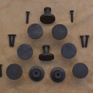 Könnte beinhalten: Ein Satz mit 10 schwarzen Metall-Schrankknöpfen mit Schrauben. Die Knöpfe sind rund und haben eine leicht erhöhte Mitte. Die Schrauben sind silberfarben.