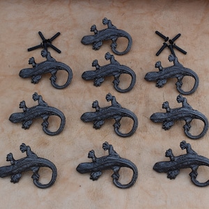 Peut inclure: Dix crochets muraux en fonte de fer noir en forme de lézard. Chaque crochet est en forme de lézard avec une queue enroulée. Les crochets sont conçus pour être montés sur un mur.