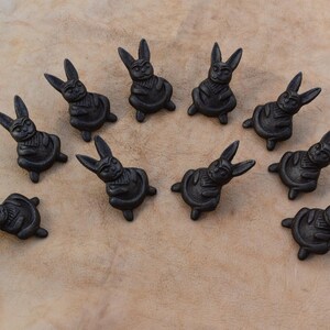 May include: A set of ten black ceramic rabbit figurines, each sitting in a meditative pose with their paws folded in front of them. The rabbits are arranged in a circle on a light brown surface.
