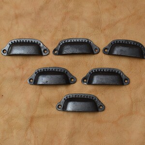 May include: Six black metal drawer pulls with a decorative beaded edge. The pulls are all the same size and shape, and they are arranged in a staggered pattern.