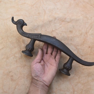 May include: A black metal door handle shaped like a stylized peacock with intricate details. The handle has two decorative bases.