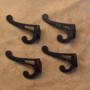 May include: Four black cast iron hooks with a decorative design. The hooks are arranged in a square pattern on a light brown surface.