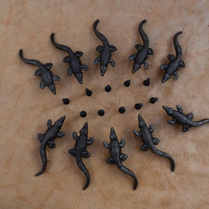 May include: A circle of black alligator figurines on a light brown surface. The alligators are arranged in a circle with their tails pointing outwards.