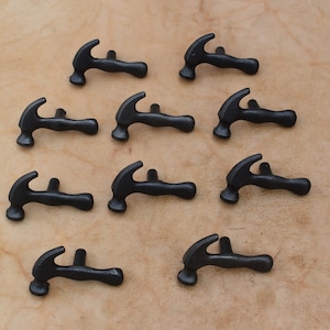 May include: Twelve black metal hammer-shaped drawer pulls. The pulls are arranged in three rows of four. The pulls are all the same size and shape.