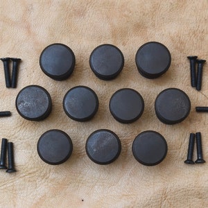 May include: Ten black metal cabinet knobs with a smooth, slightly textured finish. The knobs are arranged in two rows of five, with a set of screws next to each row.