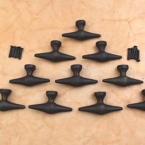 May include: Ten dark grey, T-shaped cabinet pulls arranged in a triangle, with two small groups of screws. The pulls have a rounded top and a flat, horizontal bar. The background is a light brown, textured surface.