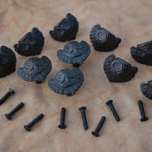 May include: Ten black metal owl-shaped cabinet knobs with a decorative design and ten black screws.