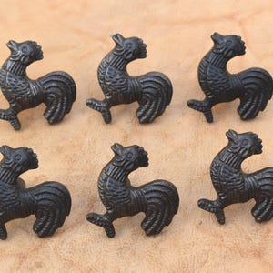May include: A set of six black metal cabinet knobs, each shaped like a rooster in profile. The roosters feature textured detailing on the feathers and body, with a raised head and a curved tail. These hardware pieces are uniform in design.