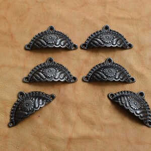May include: Six black cast iron drawer pulls with a decorative floral design. Each pull is shaped like a half-circle with a scalloped edge.