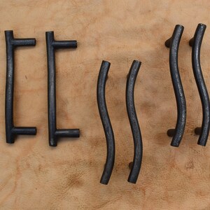 May include: Set of six black metal cabinet pulls. Two are straight with a T-shaped end and four are curved.