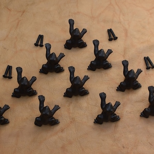 May include: Ten black cast iron frog drawer pulls with screws. The frogs are in a variety of poses with their legs raised.