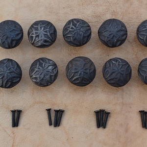 Könnte beinhalten: Zwölf schwarze Metall-Schrankknöpfe mit einem dekorativen keltischen Knotendesign. Jeder Knopf hat einen Durchmesser von etwa 2,5 cm. Die Knöpfe sind in drei Reihen zu vier angeordnet, mit drei Sätzen Schrauben im Lieferumfang enthalten.