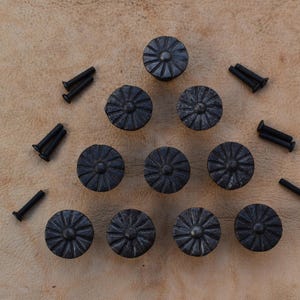 May include: A set of 10 black metal cabinet knobs with a decorative floral design. The knobs are arranged in a triangular pattern on a light brown surface.