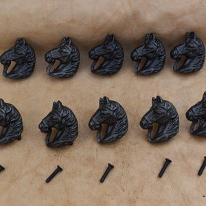May include: Ten black metal horse head drawer pulls with screws. The horse heads are detailed and have a rustic look.