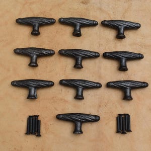 May include: A collection of ten T-shaped cabinet knobs with a dark, textured, twisted metal finish. The knobs are arranged in rows, accompanied by two sets of four small black mounting screws positioned at the bottom of the display.