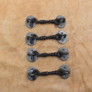 May include: Four dark gray metal cabin hooks arranged in a vertical column. Each hook features a central rod with decorative ridges, connected to two oval-shaped mounting plates, each containing two small circular screw holes for installation.
