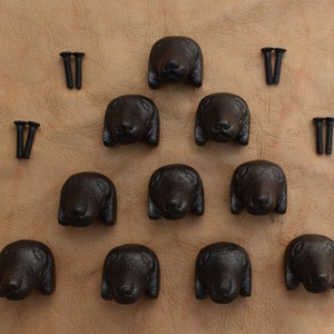 Op de afbeelding: Twaalf zwarte gietijzeren trekknoppen voor lades in de vorm van een teckelkop met schroeven.