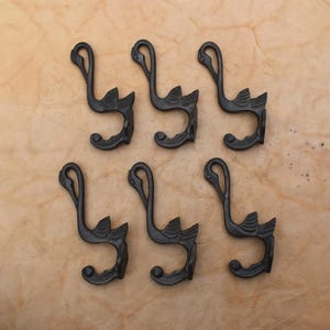 Puede incluir: Un juego de seis ganchos de pared de metal marrón oscuro, cada uno con forma de cisne estilizado con un cuello largo y un cuerpo curvado. Los ganchos están dispuestos en dos filas de tres, con un acabado mate liso y una silueta elegante.