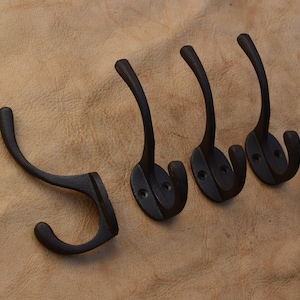 May include: Four black metal hooks with a double hook design. The hooks are mounted on a brown surface.