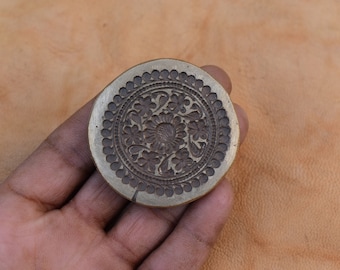 May include: A round brass stamp with a floral design. The stamp is about 2 inches in diameter and has a raised design of flowers and leaves.