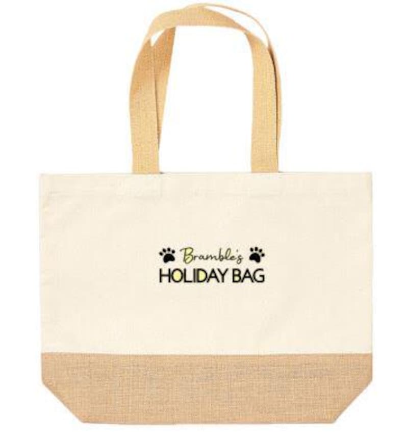 May include: A beige canvas tote bag with a brown jute bottom. The bag has black paw prints and the text "Bramble's HOLIDAY BAG" in yellow.