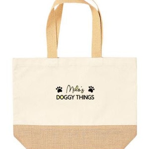 May include: A beige canvas tote bag with brown jute trim. The bag has two brown fabric handles and features black paw prints and the text "Milo's Doggy Things" in black.